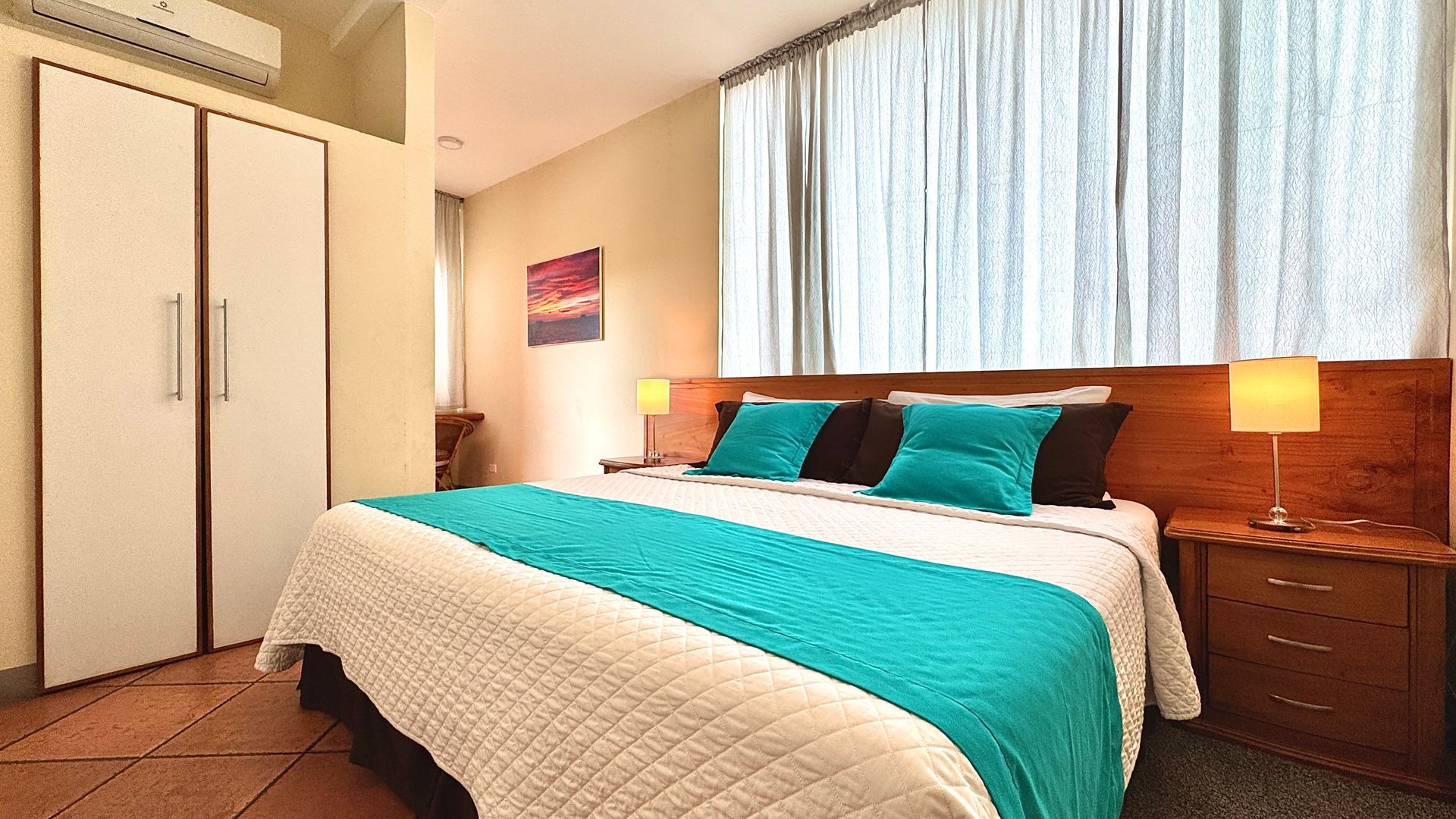 Galapagos hotel Bedroom with a large bed covered in white and teal bedding, flanked by nightstands with lamps.