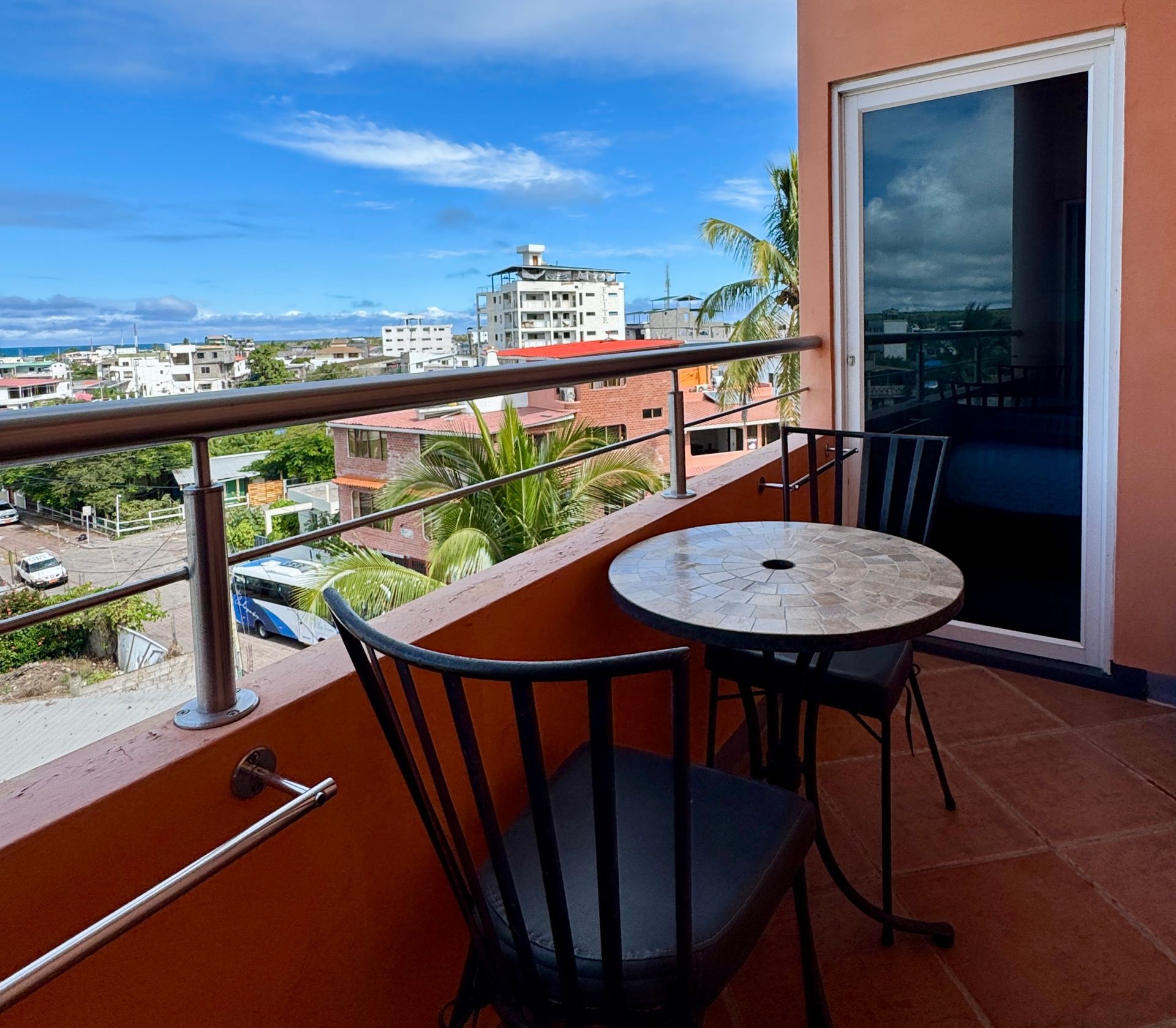 A hotel Balcony with round table and chairs overlooking city skyline and ocean under blue sky in the Galapagos.