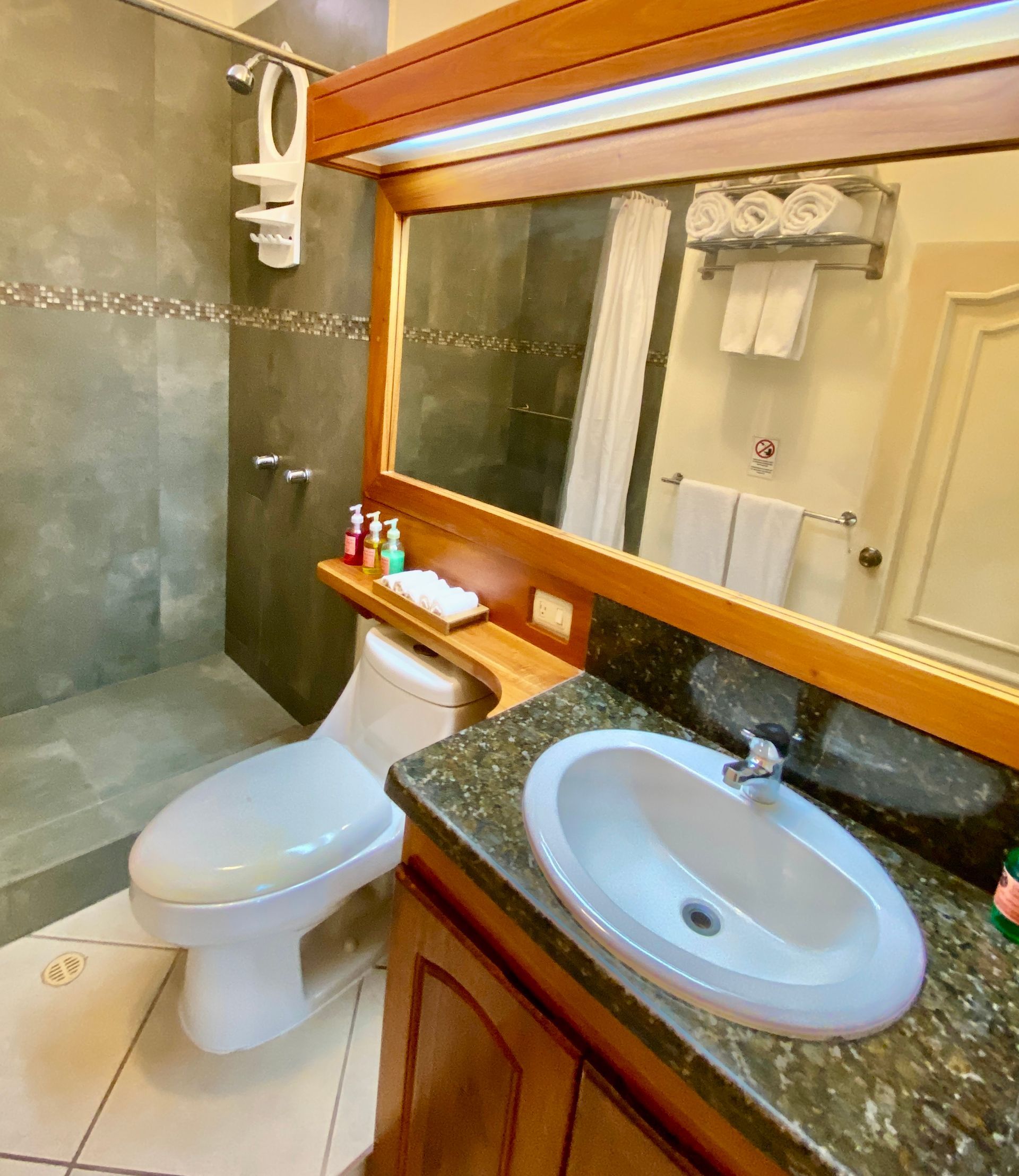 A Galapagos hotel bathroom with toilet, sink, and shower, featuring wood trim and granite countertop.