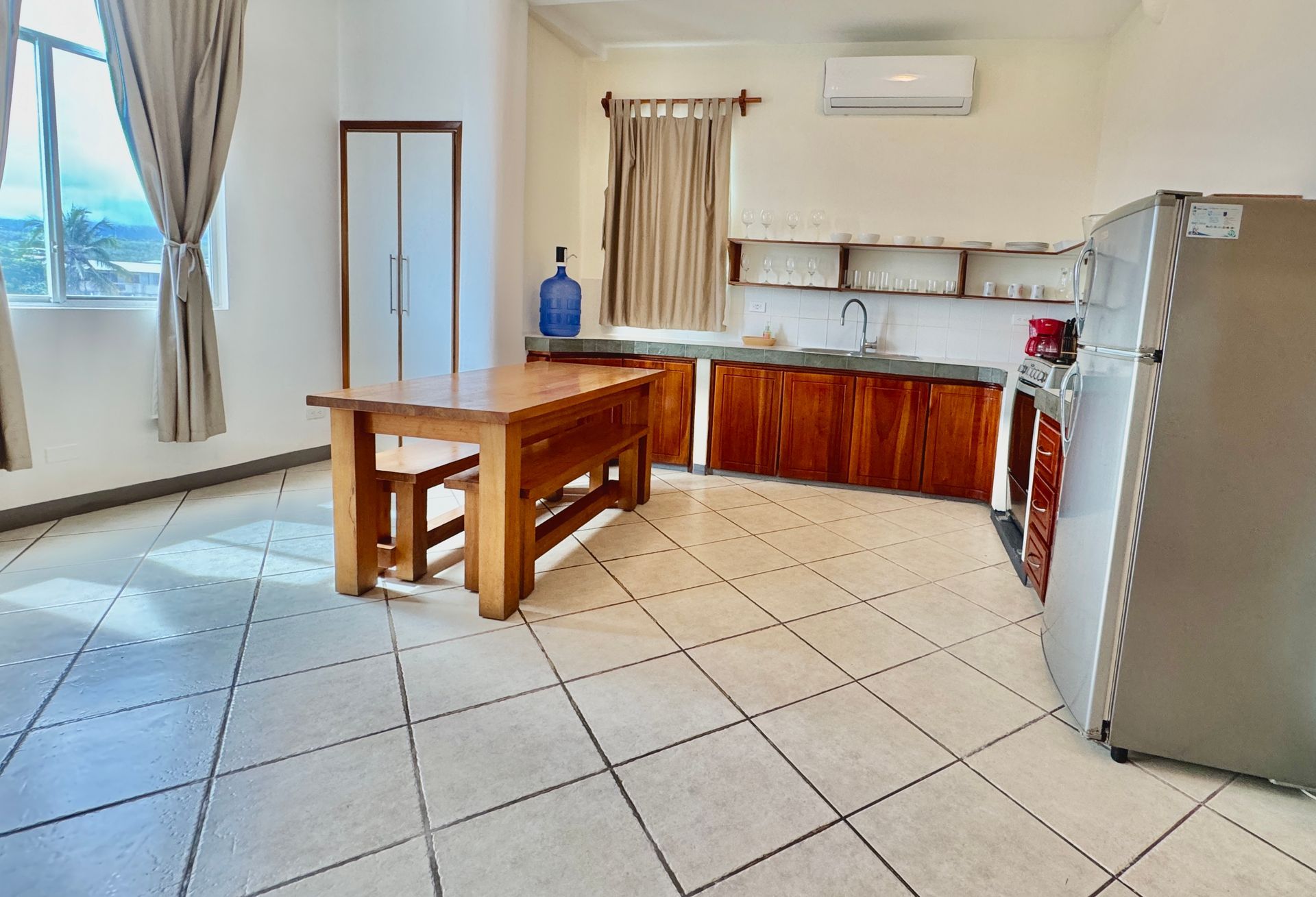 A Galapagos hotel bright kitchen with a wooden table, cabinets, and a refrigerator. Natural light streams through a window.