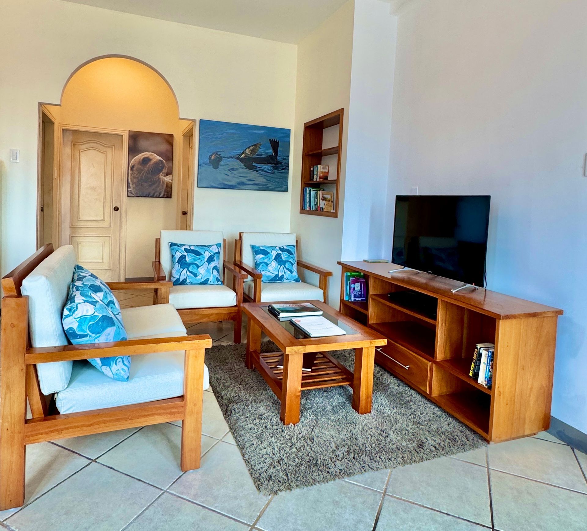A Galapagos Hotel Living room with wooden furniture, including a sofa, armchairs, and a TV console. Blue and white cushions add pops of color.