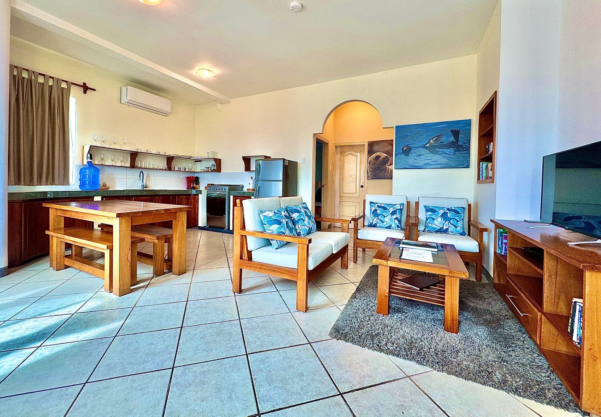 Bright Galapagos Hotel living room with tiled floor, wooden furniture, blue cushions, and an open kitchen area.