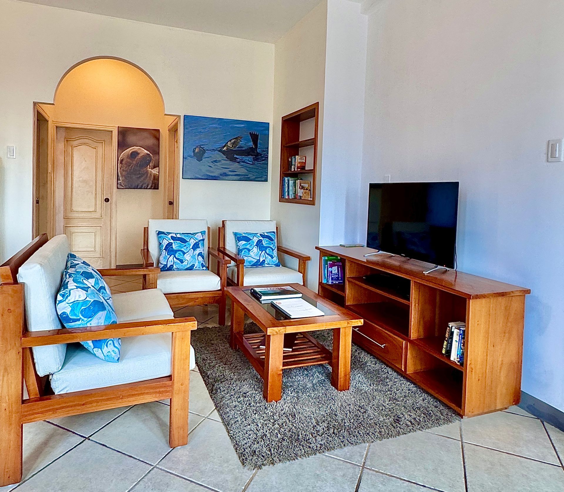 A Galapagos hotel Living room with wooden furniture, including a sofa, chairs, and a TV console, a bookshelf, and paintings.