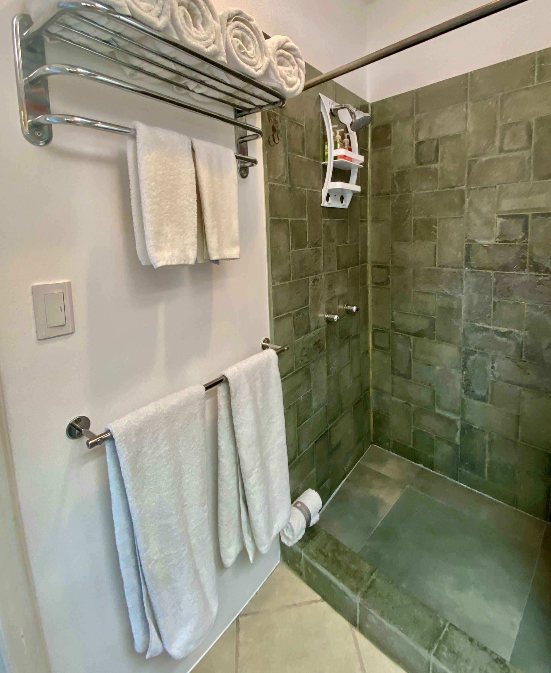 A Galapagos hotel tiled bathroom shower with towel racks, and a wall-mounted shelf.