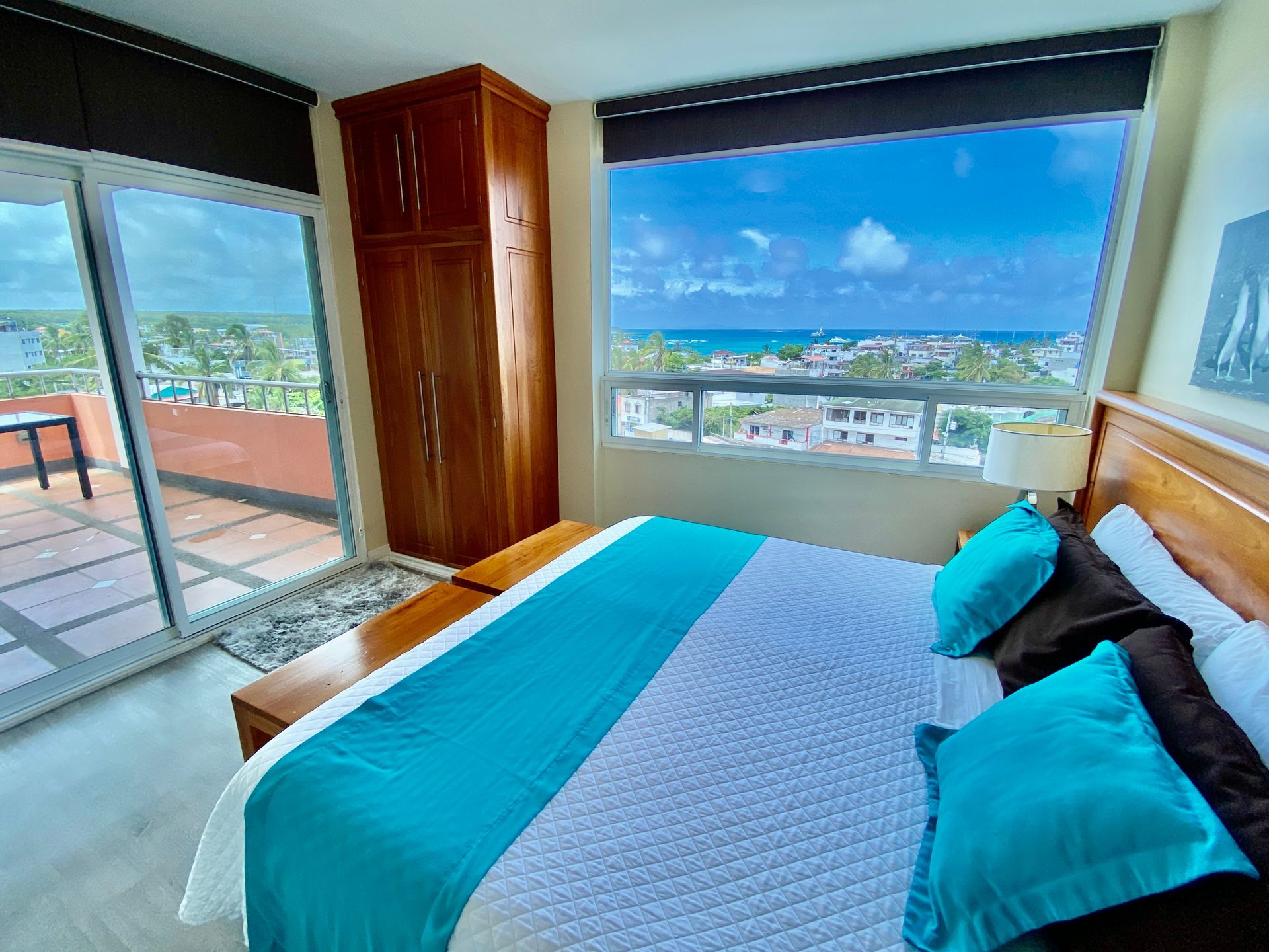Galapagos Hotel room with blue bed, wooden headboard, and large window overlooking a bright coastal cityscape in the Galapagos Islands.