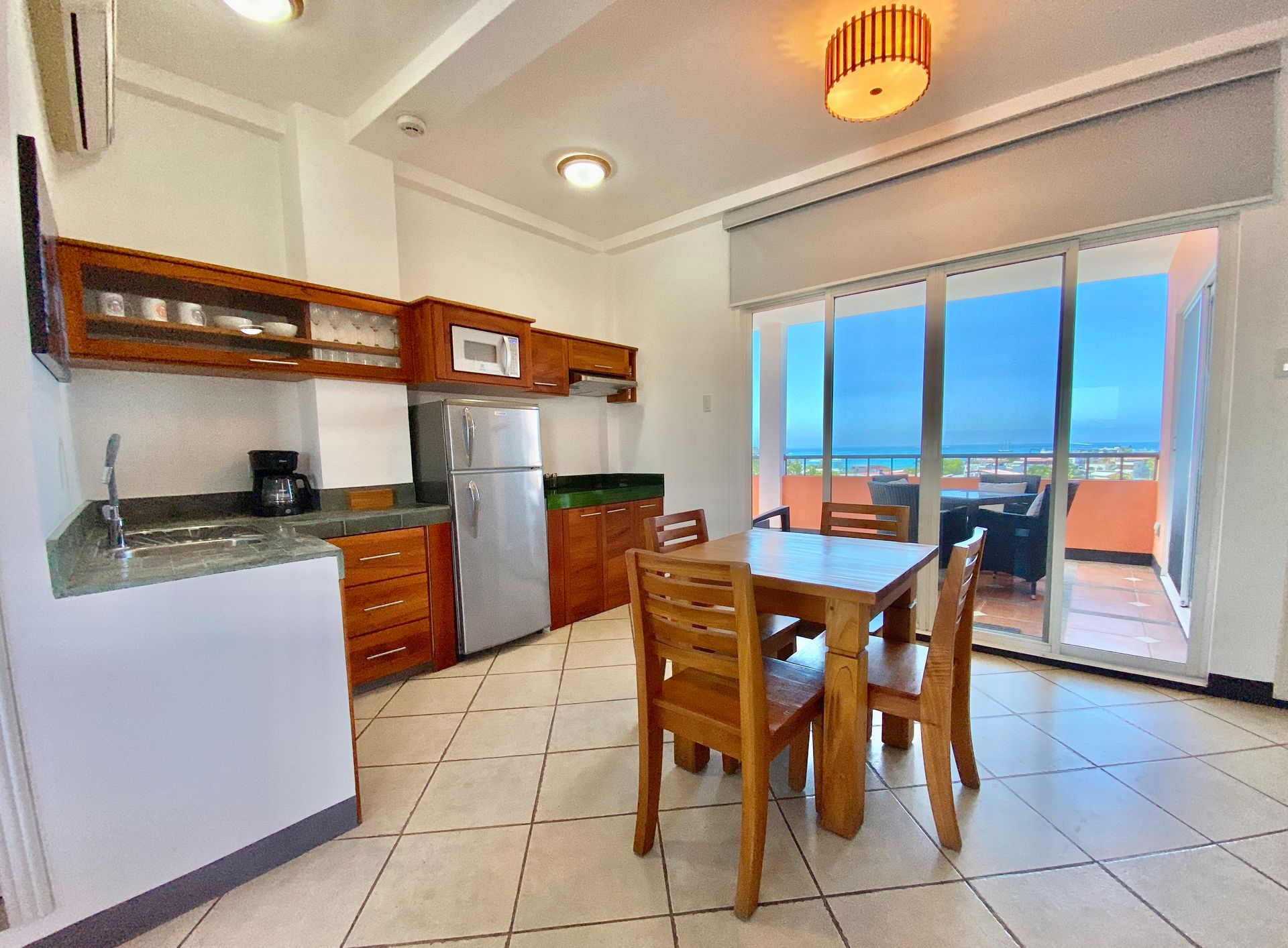 Bright Galapagos hotel kitchen with wooden table, stainless fridge, tiled floor, and ocean-view sliding doors.