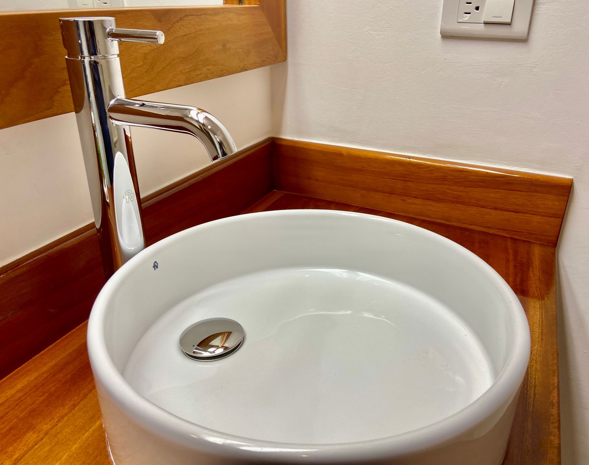 Galapagos hotel Chrome faucet over a white round sink in a wooden bathroom vanity.