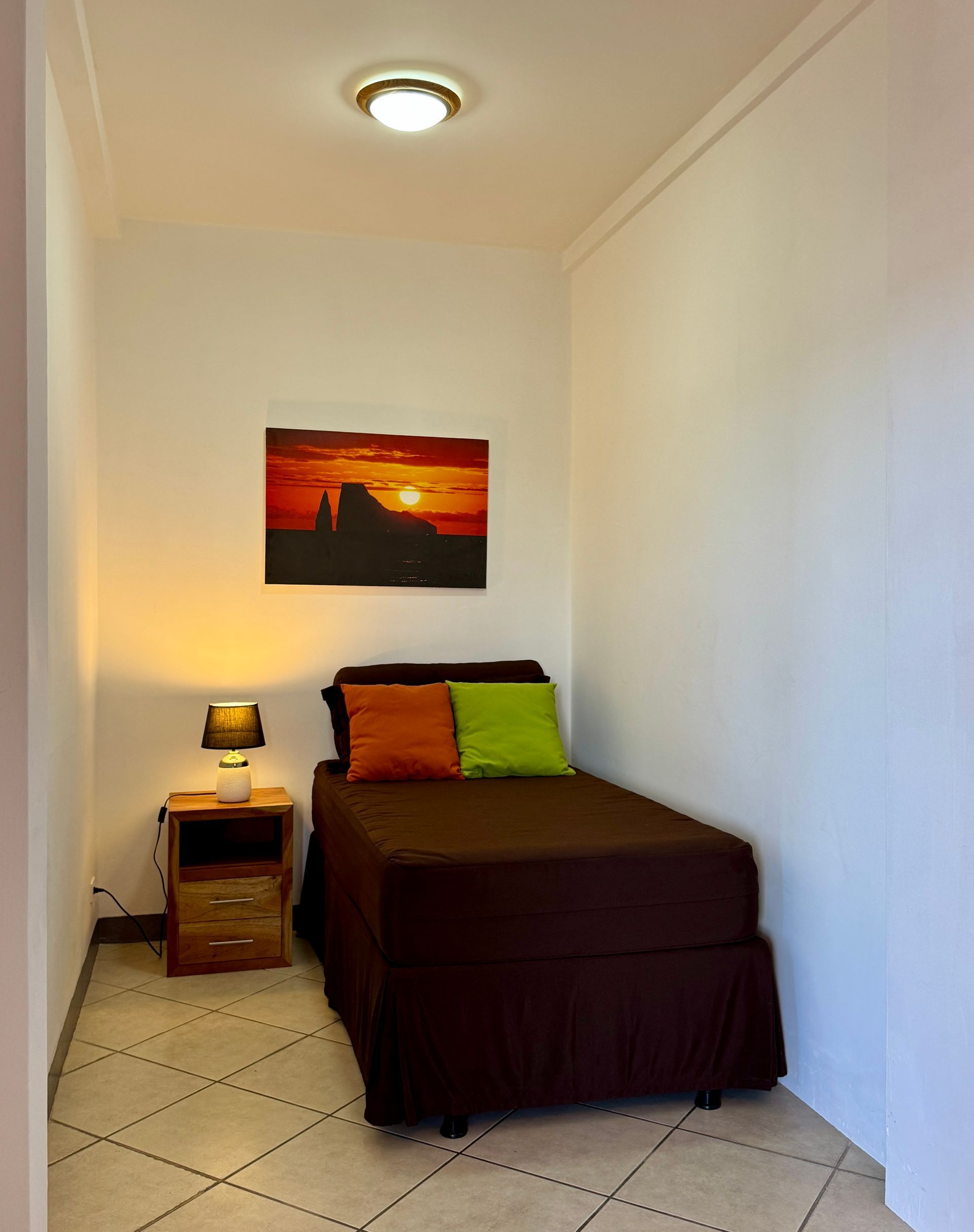 Galapagos hotel suite an additional bedroom with a single bed, bedside table, sunset wall art, and white tiled floor.