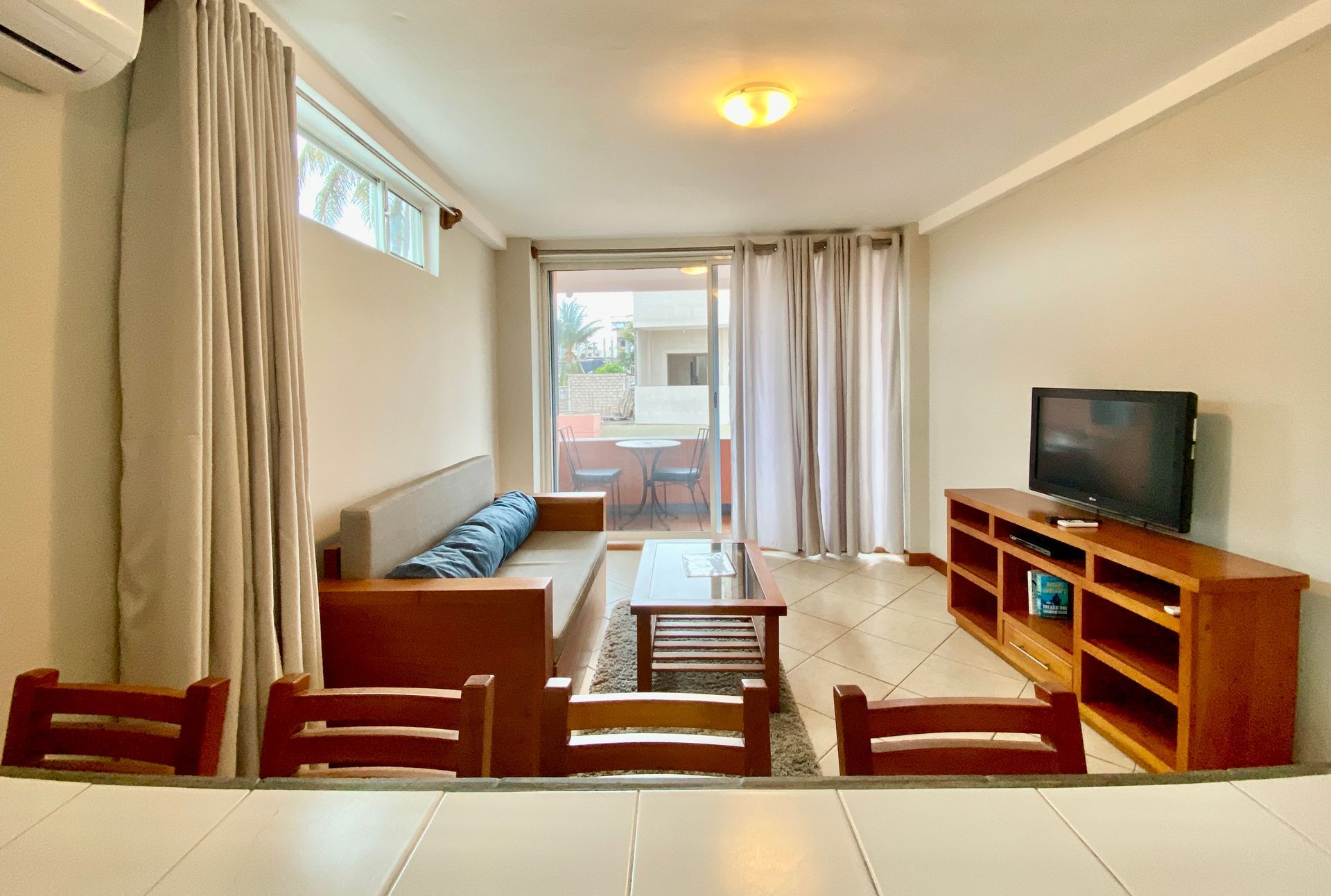 Bright hotel living room with sofa, TV, wooden table, and sliding doors to a balcony in the Galapagos Islands.