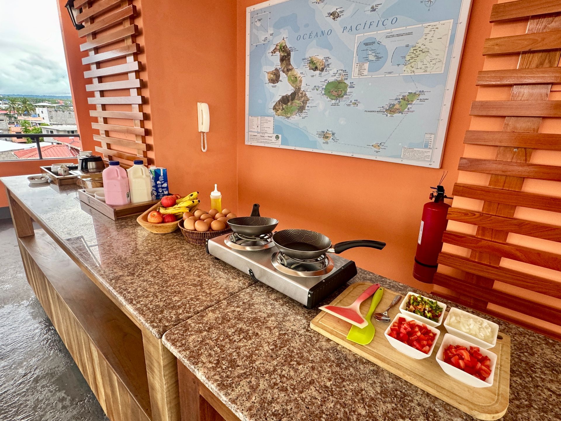 Galapagos hotel Outdoor buffet counter with hot dishes, fruit, and condiments against an orange wall and map