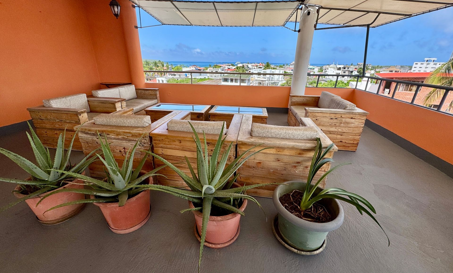 Rooftop Hotel terrace with stone seating, potted succulents, and orange walls under a canopy. in the Galapagos Islands.