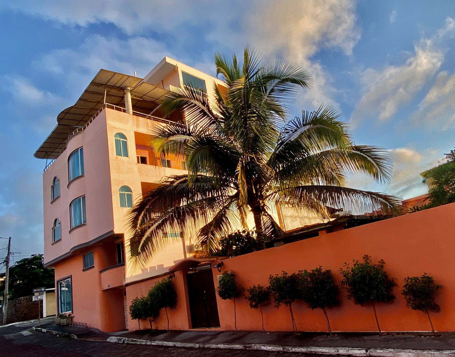 Peach house with palm tree beside an orange wall under a partly cloudy sky