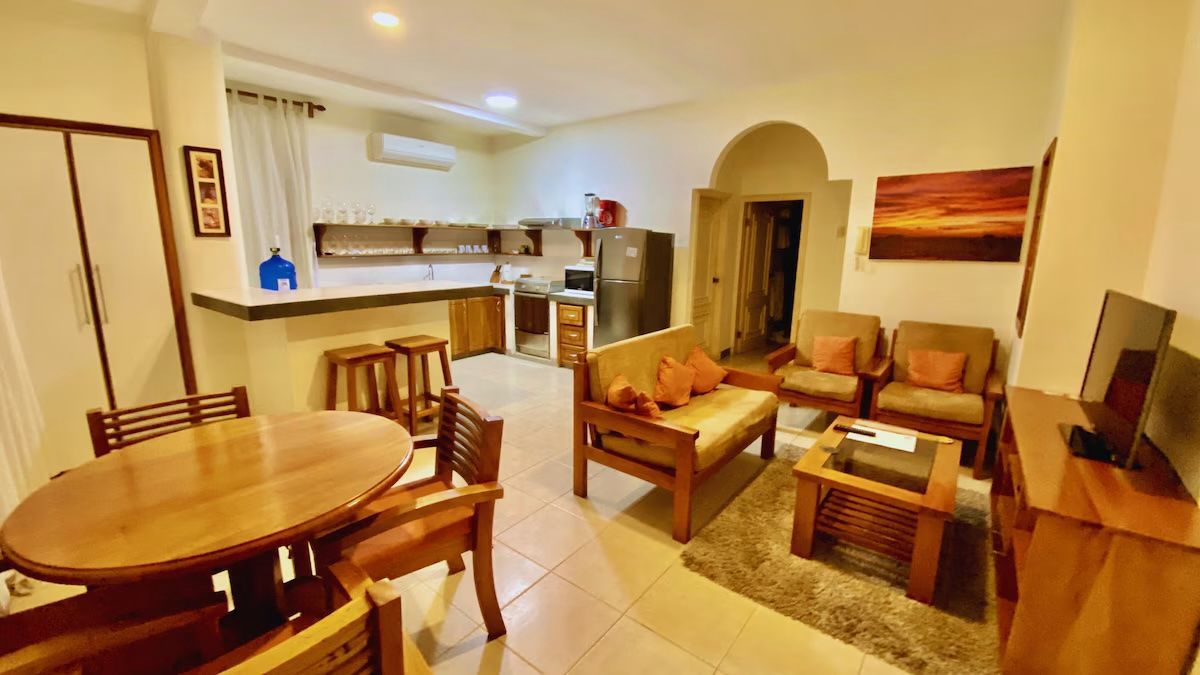 Cozy living room with sofas, coffee table, dining area, and a small kitchen bar in warm lighting