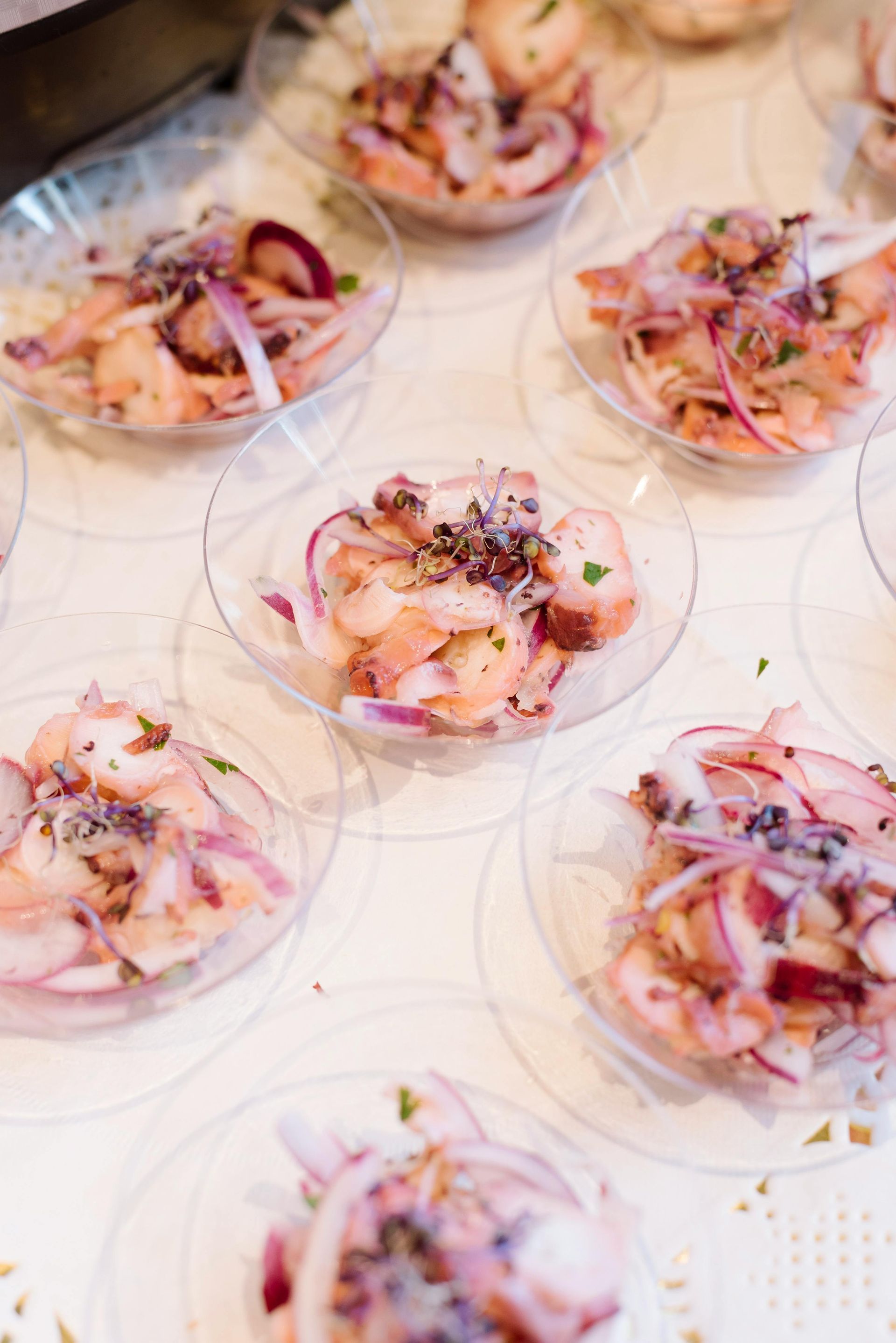 Small, clear bowls filled with ceviche, each topped with red onion and herbs, arranged on a white surface in Galapagos.