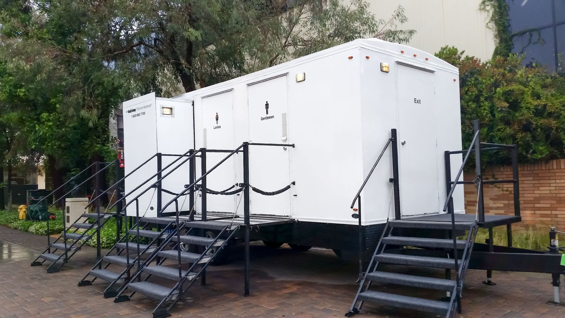White portable restroom trailer on a paved driveway, with steps leading to two separate entrances.