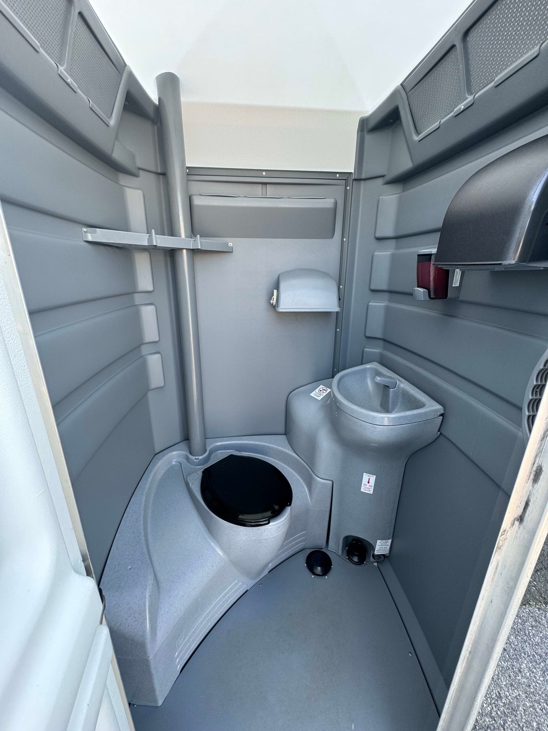 Interior of a gray portable toilet with a toilet, sink, and paper towel dispenser.