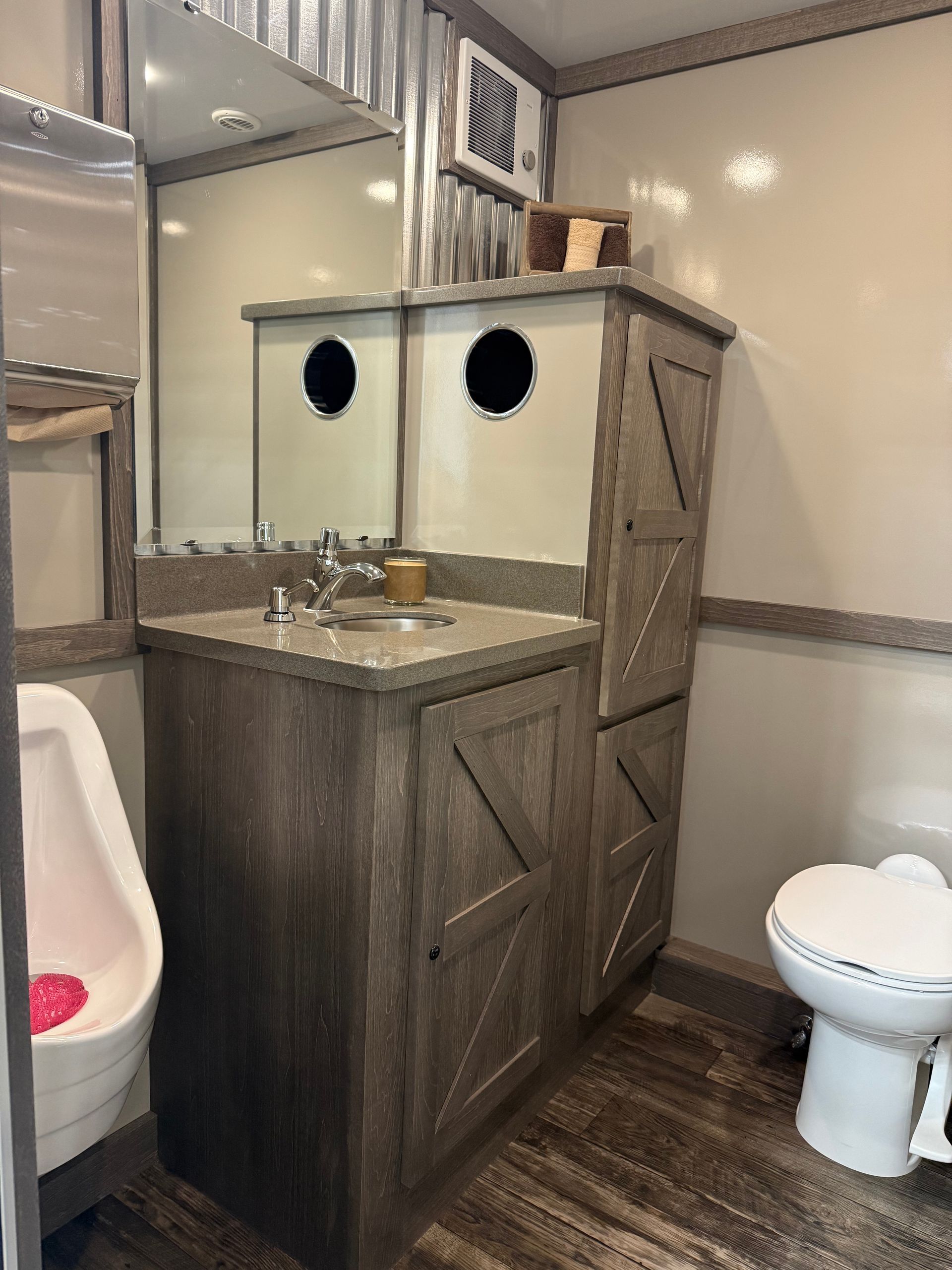 Restroom with a vanity, mirror, toilet, and urinal, featuring rustic wood cabinetry in a compact space.
