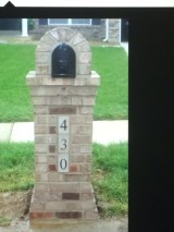 Stone mailbox post with black mailbox and house number 430 on a lawn.