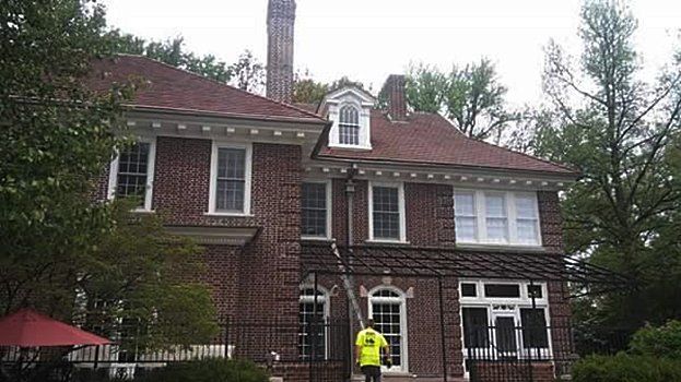 Brick house with red roof and white trim, a person in a yellow jacket standing outside.