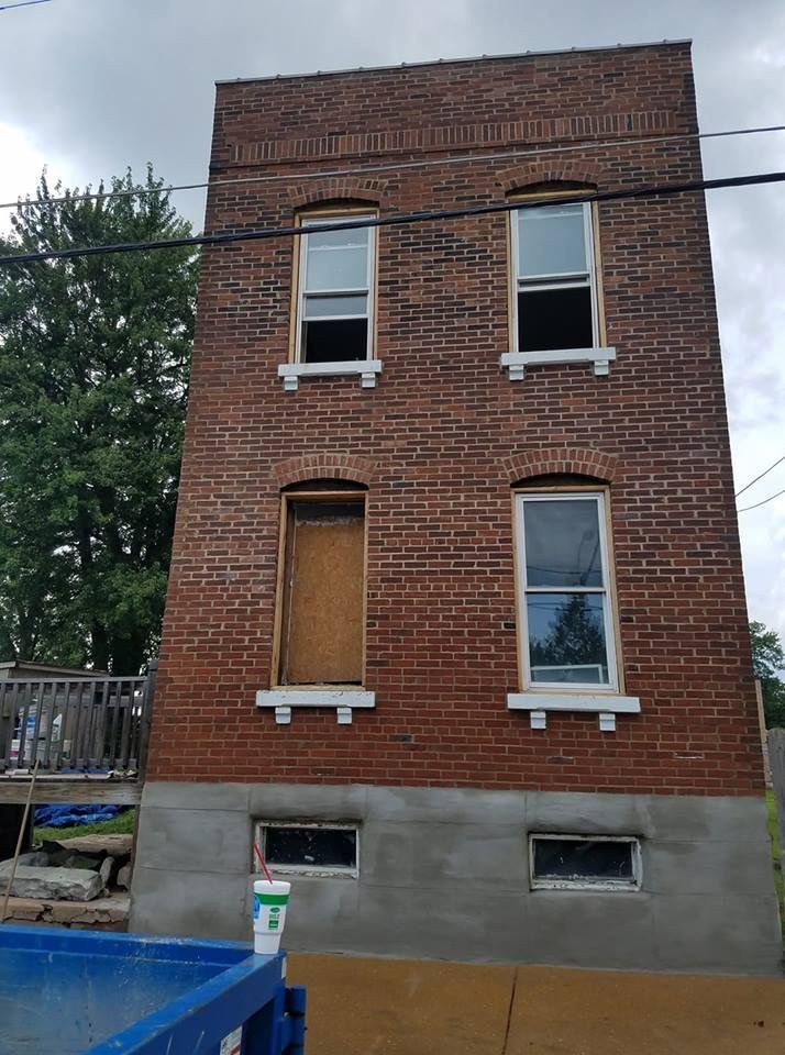 Red brick building with boarded windows and a gray concrete foundation near a blue pool