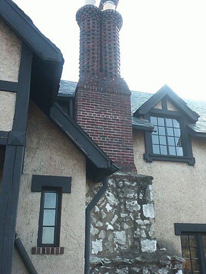 Brick chimney on a stucco house with dark trim and a stone base.