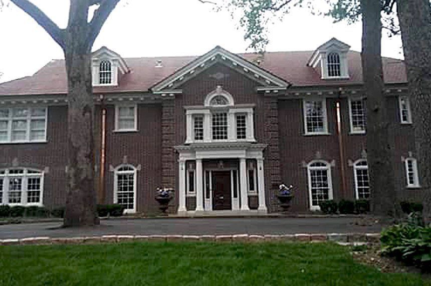 Brick mansion with white trim, arched porch, and dormer windows behind a grassy lawn