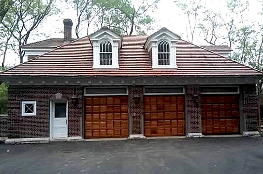 Front view of a brick garage with two wooden doors and dormer windows under a tiled roof