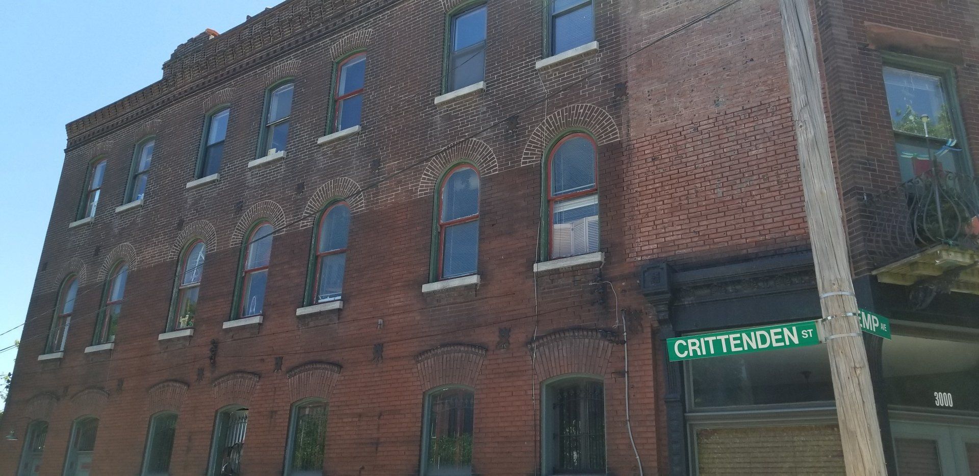 Red brick building with many windows and a green neon sign at the corner entrance