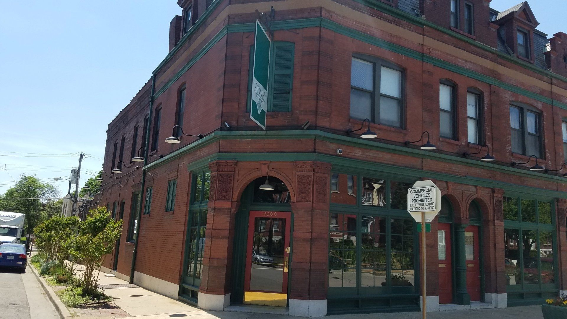 Red brick corner storefront with green trim on a sunny street corner