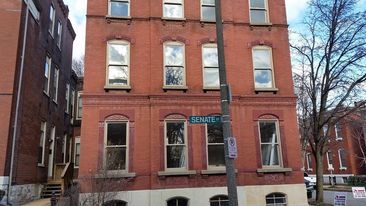 Red brick townhouse on a narrow street with a teal street sign and parked cars nearby