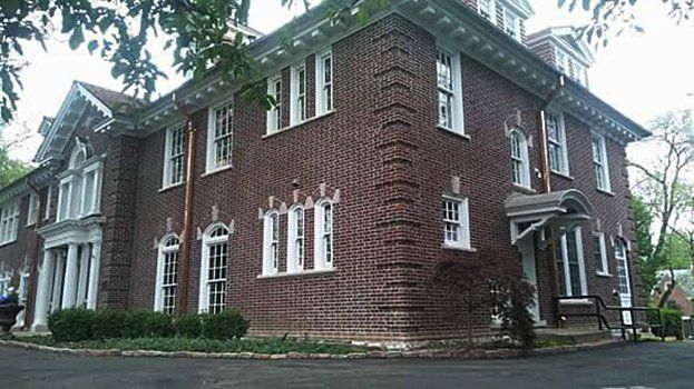 Brick colonial-style house with white-trimmed windows and a covered entrance, viewed from the street