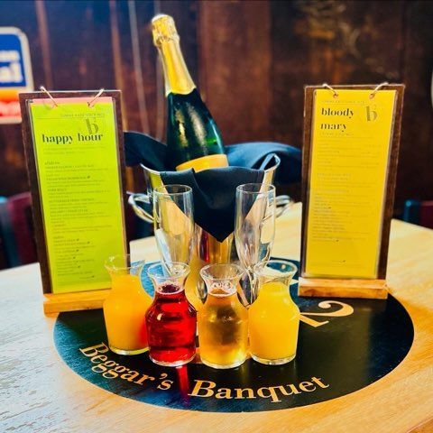 A Beggar's Banquet table with a champagne bottle in a bucket, two menu signs, two empty flutes, and four small carafes.