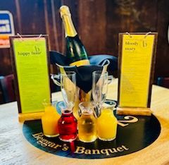 A bottle of champagne in an ice bucket, two empty flutes, and four small carafes of juice on a Beggar’s Banquet tabletop.
