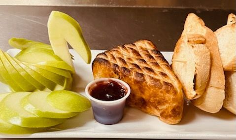 A plate with sliced green apples arranged like a swan, a grilled cheese sandwich, a small cup of jam, and toasted bread.