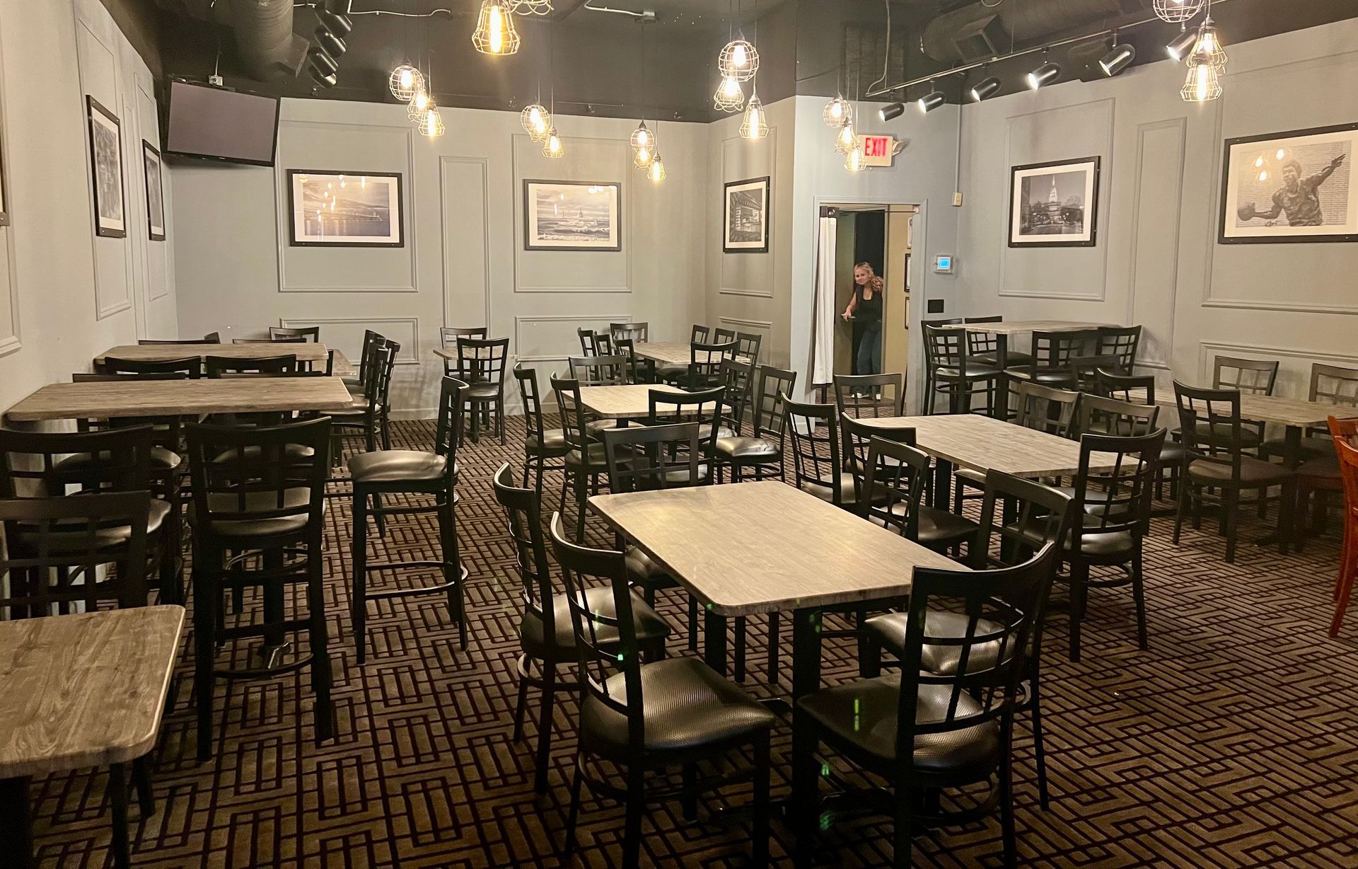An empty dining area with multiple tables and chairs, wood-paneled walls, hanging globe lights, and patterned carpet.