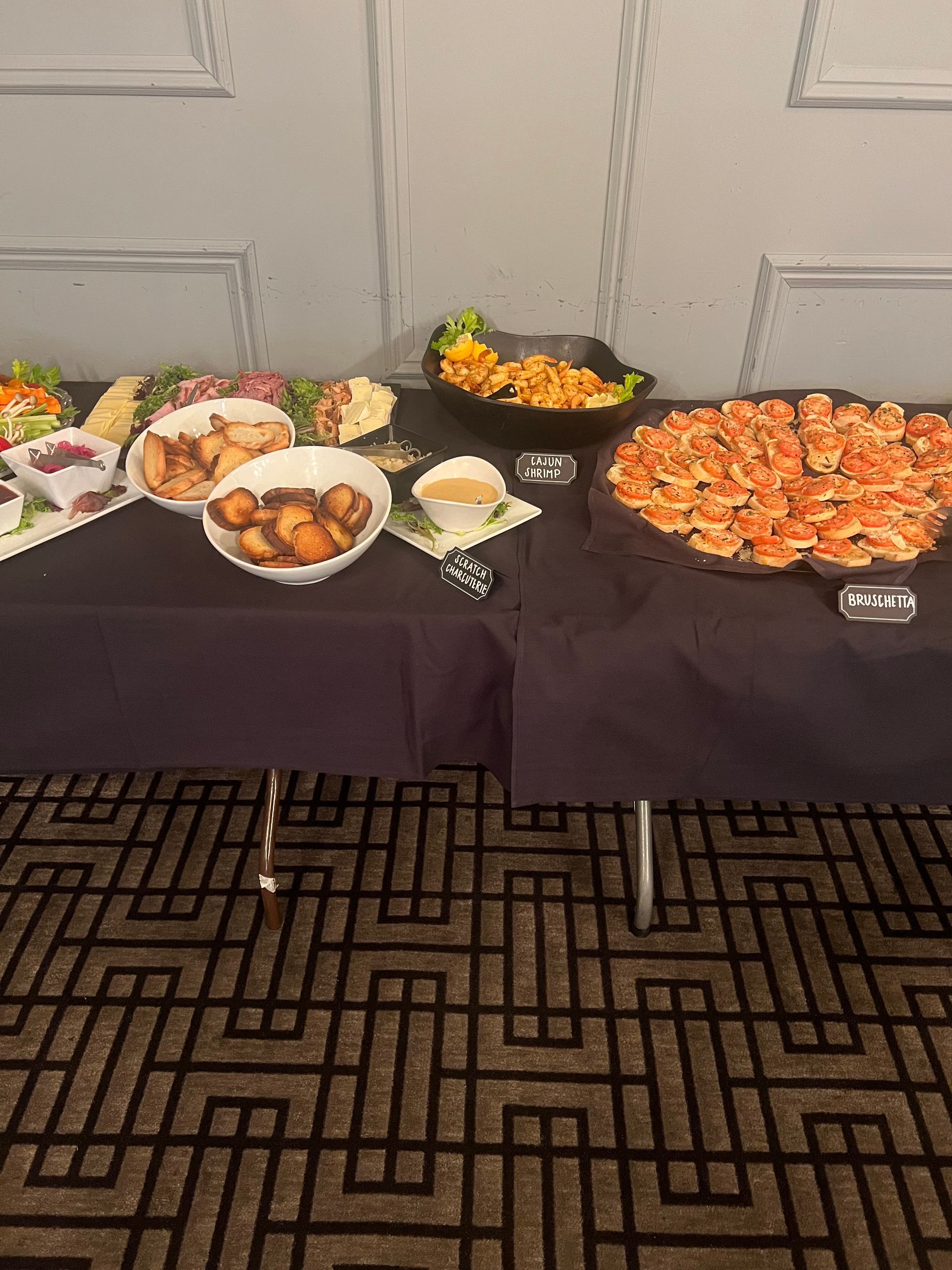 A buffet table covered in a dark tablecloth holds several bowls of appetizers and a large platter of toasted bread slices.