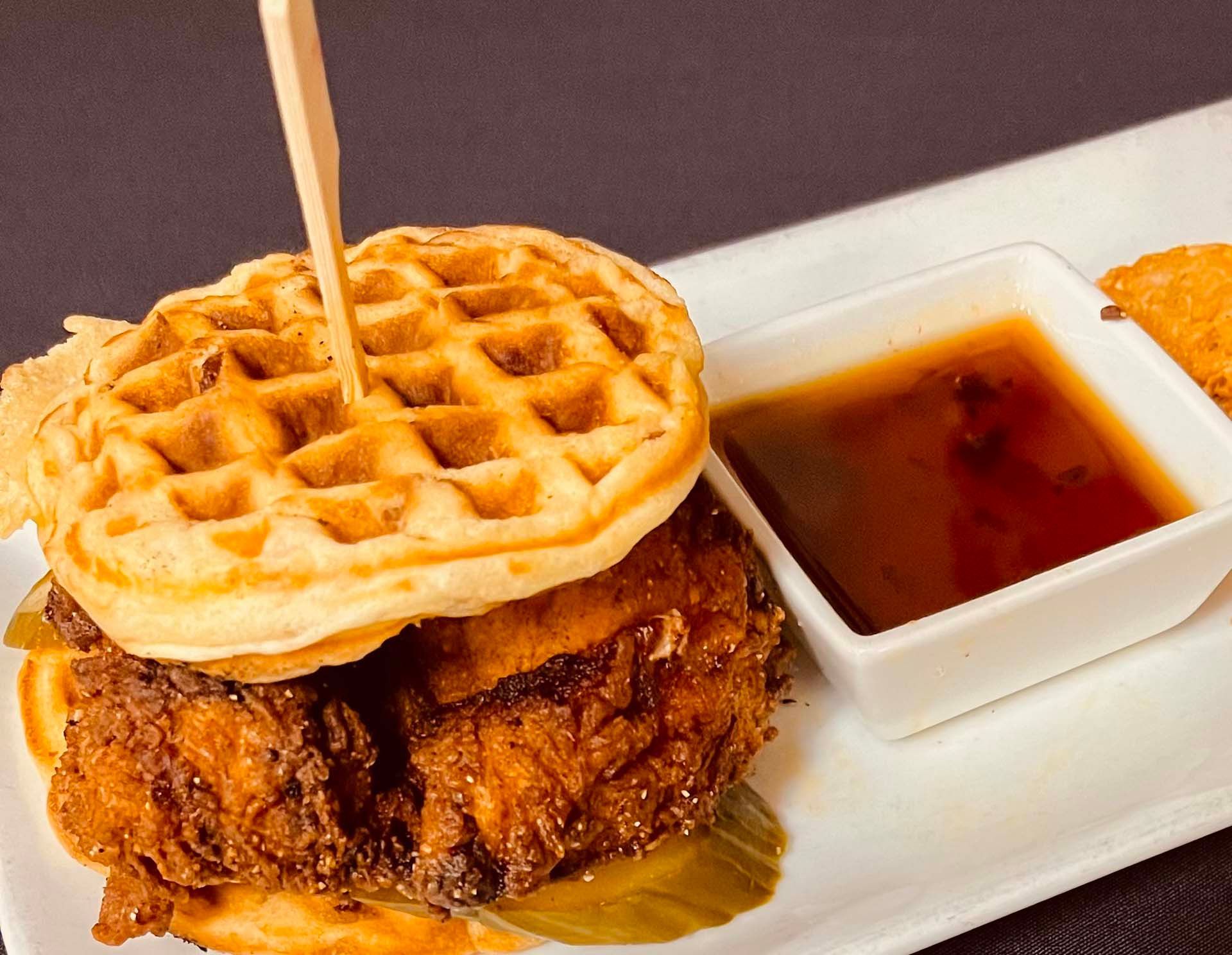 A chicken and waffle sandwich with syrup on a white plate