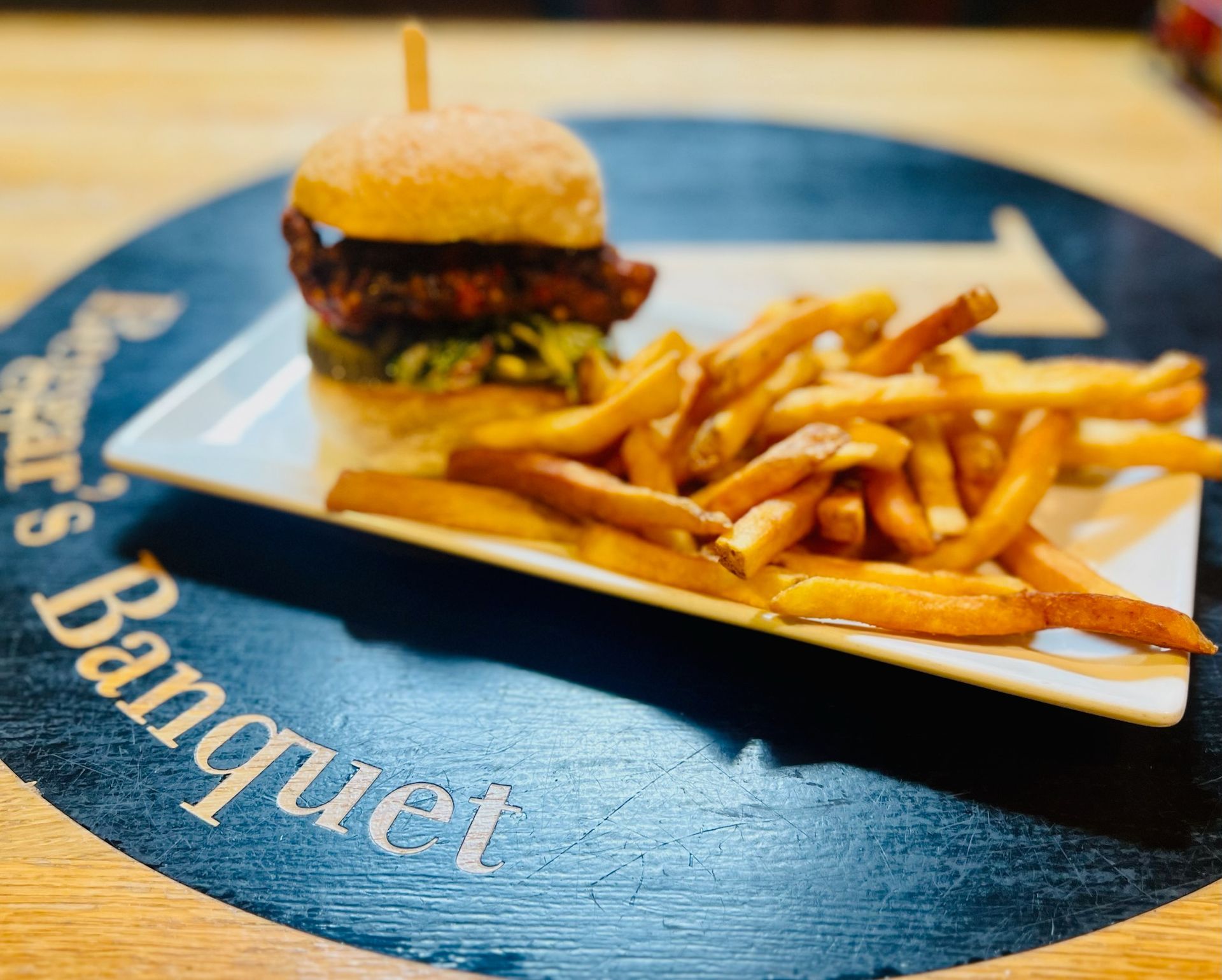 A burger and a side of golden-brown fries served on a white rectangular plate atop a round black table mat.