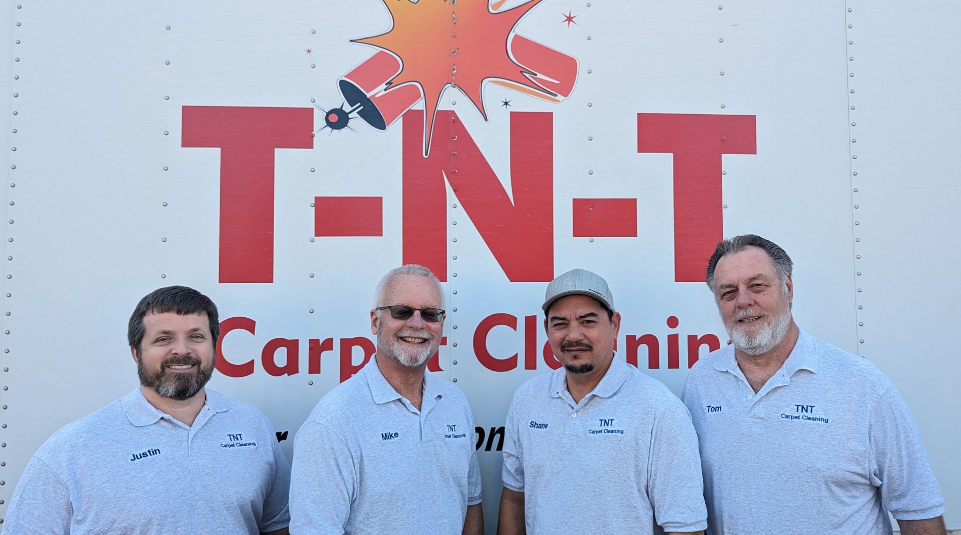Four men in matching shirts in front of a white truck with 