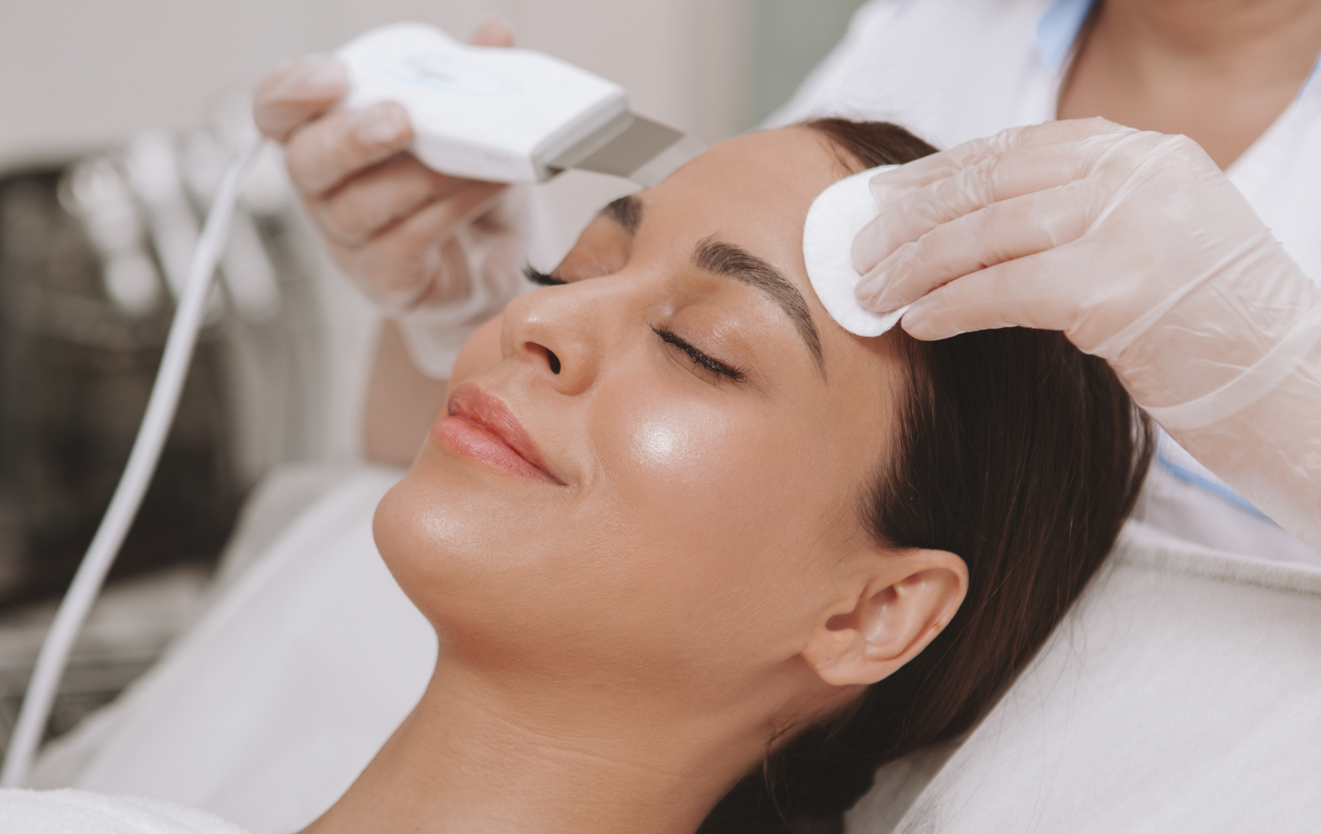 Facial treatment with a gloved aesthetician using a handheld device on a relaxed client