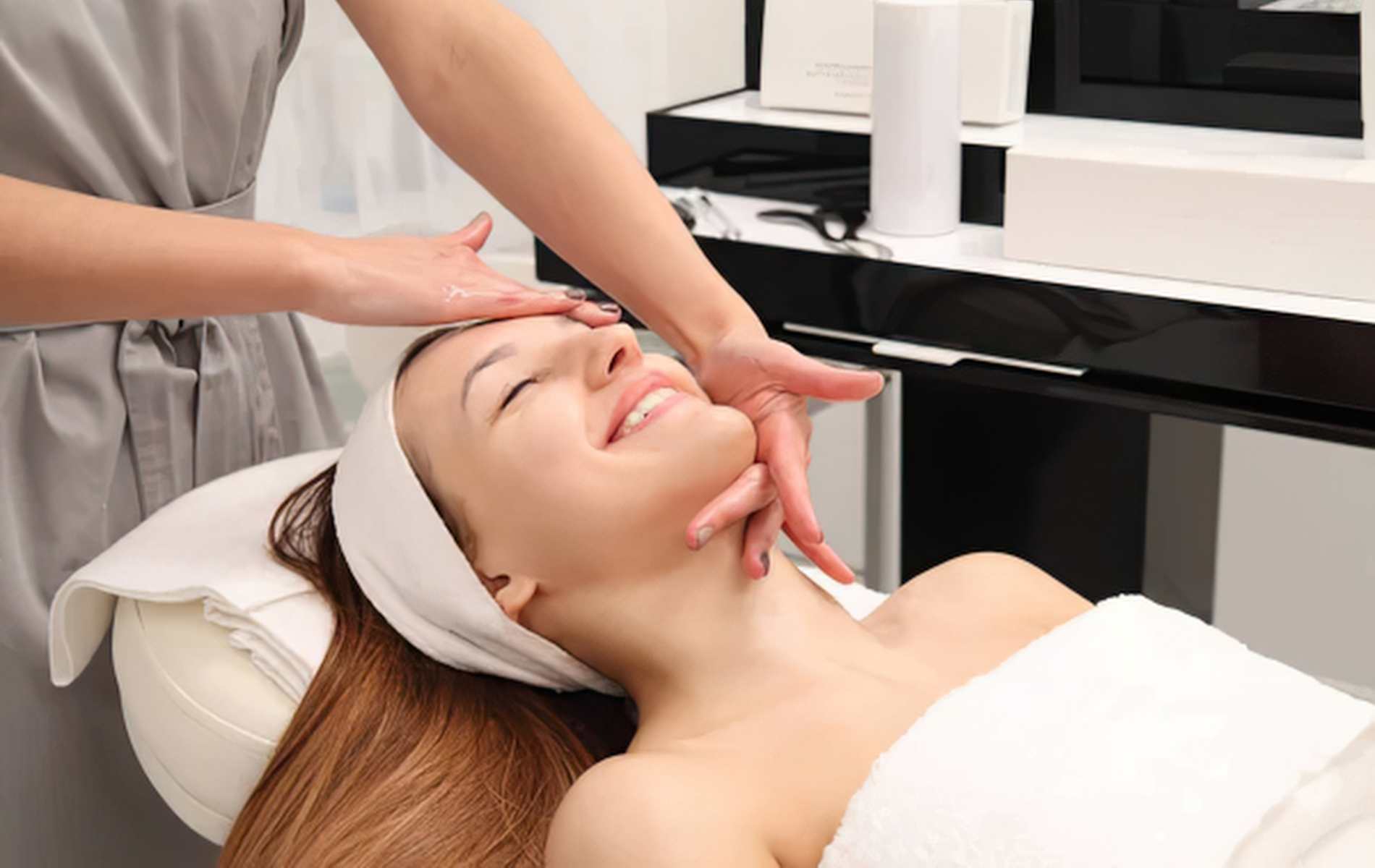 Facial treatment with a woman reclining as a therapist massages her face in a spa salon