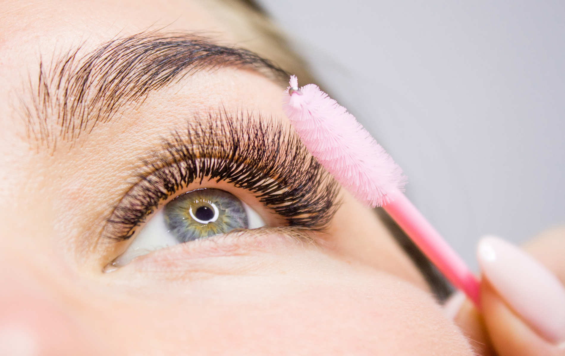 Close-up of an eye as a pink mascara wand applies makeup to the eyelashes