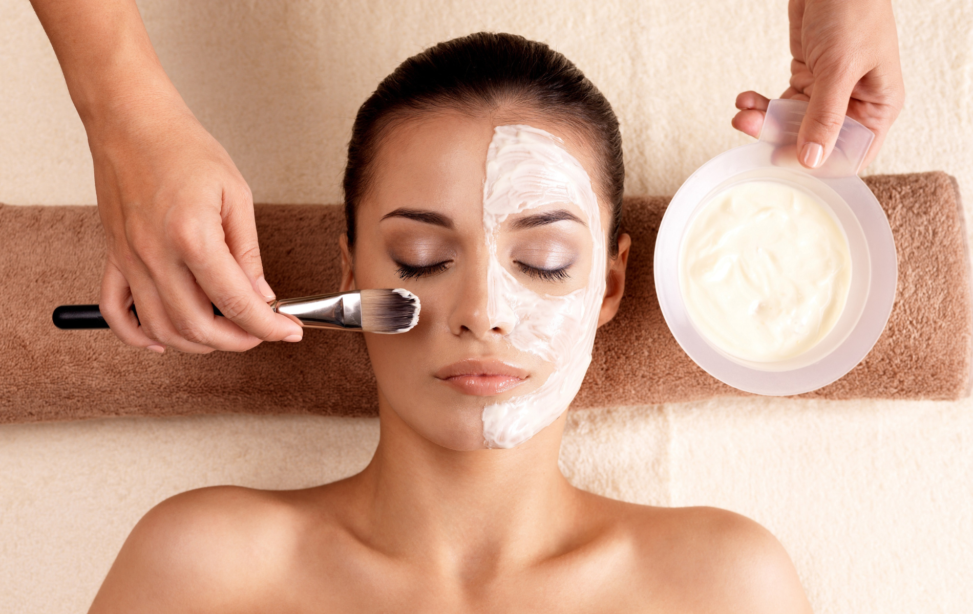 Spa facial treatment with brush applying cream to woman's face beside bowl of mask