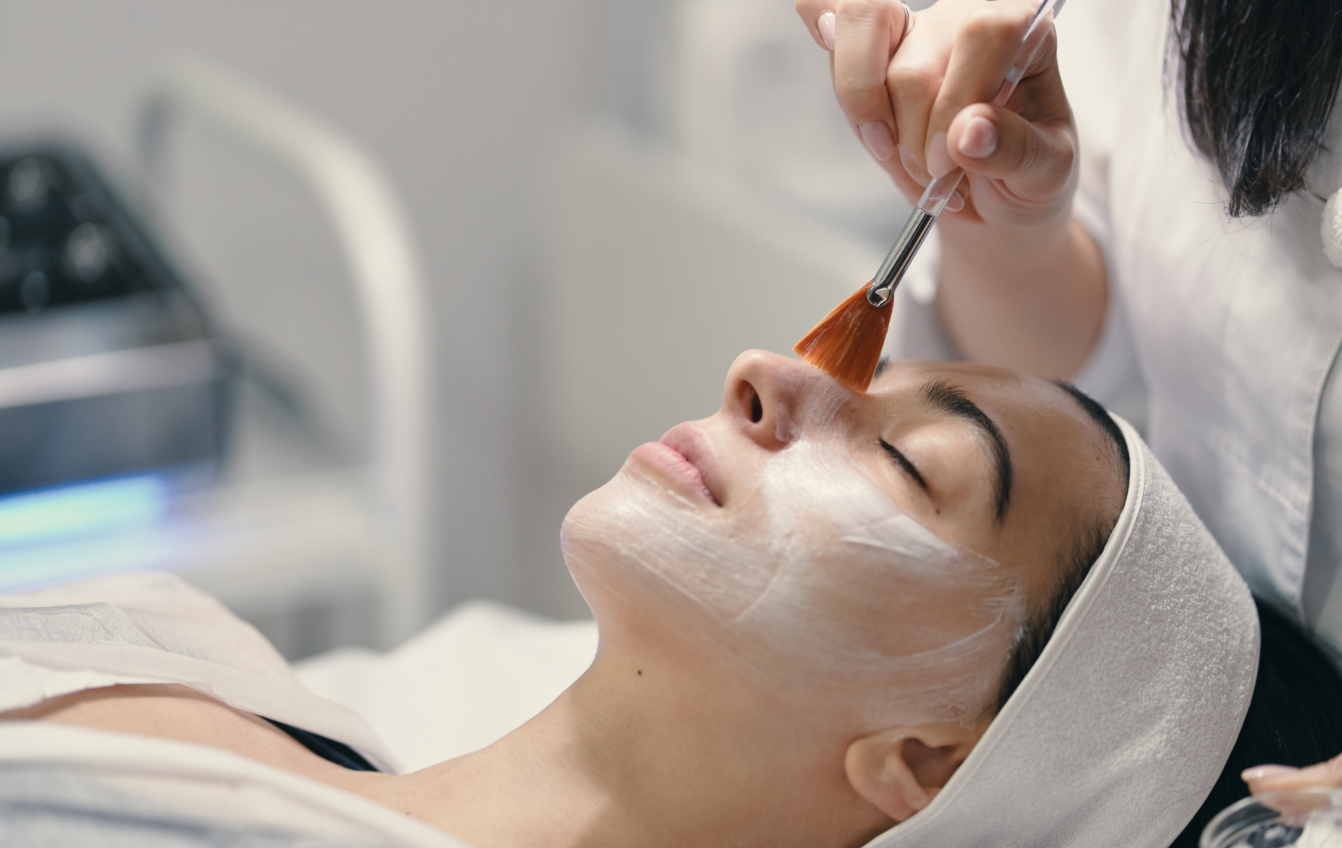 Cosmetologist applying a facial treatment with a brush to a client lying on a spa bed
