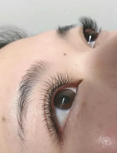 Close-up of a person’s eyes with long eyelashes and natural eyebrow hairs on a neutral background