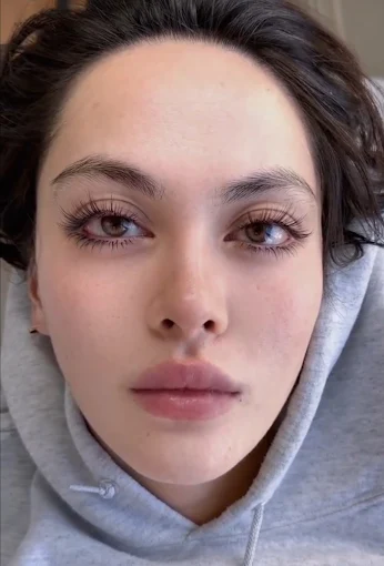Close-up portrait of a person in a gray hoodie, looking straight at the camera with a neutral expression.