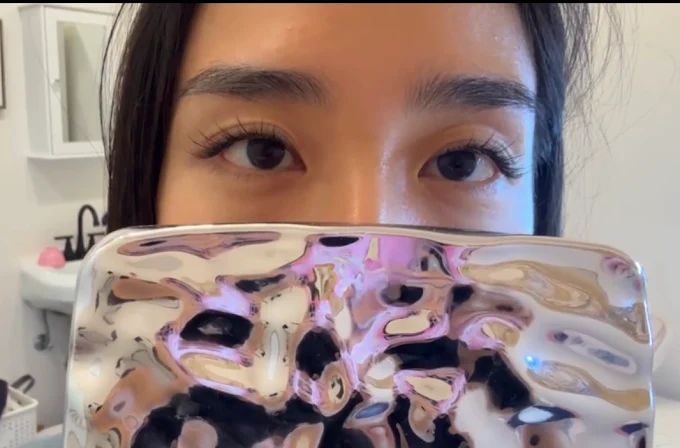 Close-up of a person peeking over a glossy iridescent phone case, showing their eyes and eyebrows.