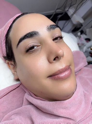 Close-up of a person in a pink head covering, reclining with a calm expression on a white bed.