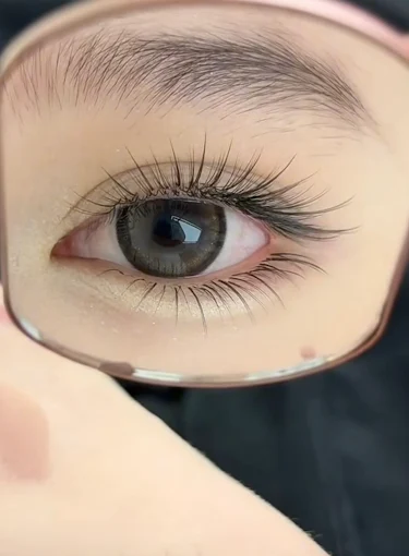 Close-up of a brown eye reflected in a handheld mirror, showing long eyelashes and a pink rim.