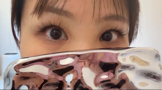 Close-up of wide eyes peeking over a shiny pink-and-silver surface